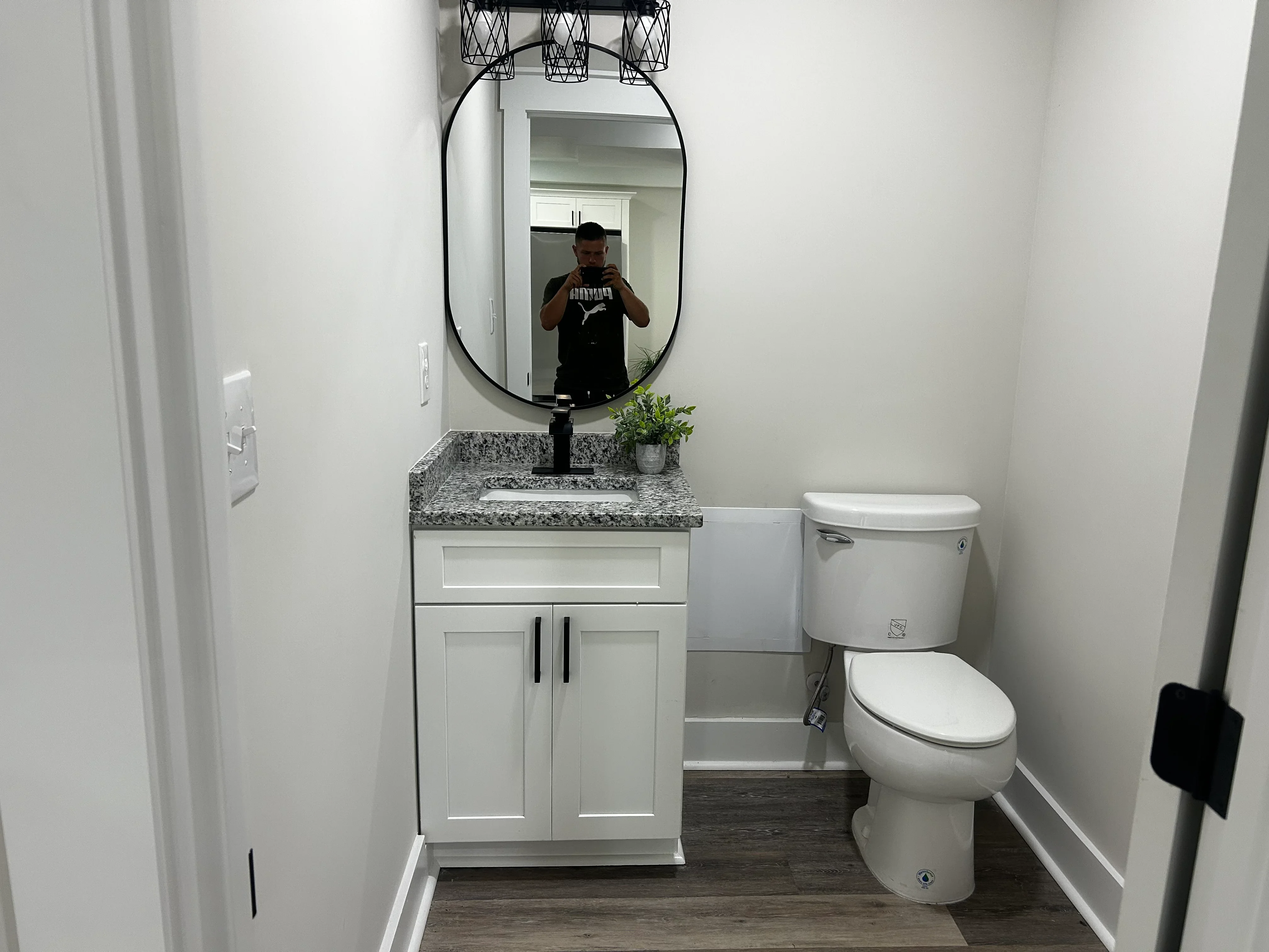 White vanity with granite countertop, black framed mirror, and two-piece toilet in renovated bathroom