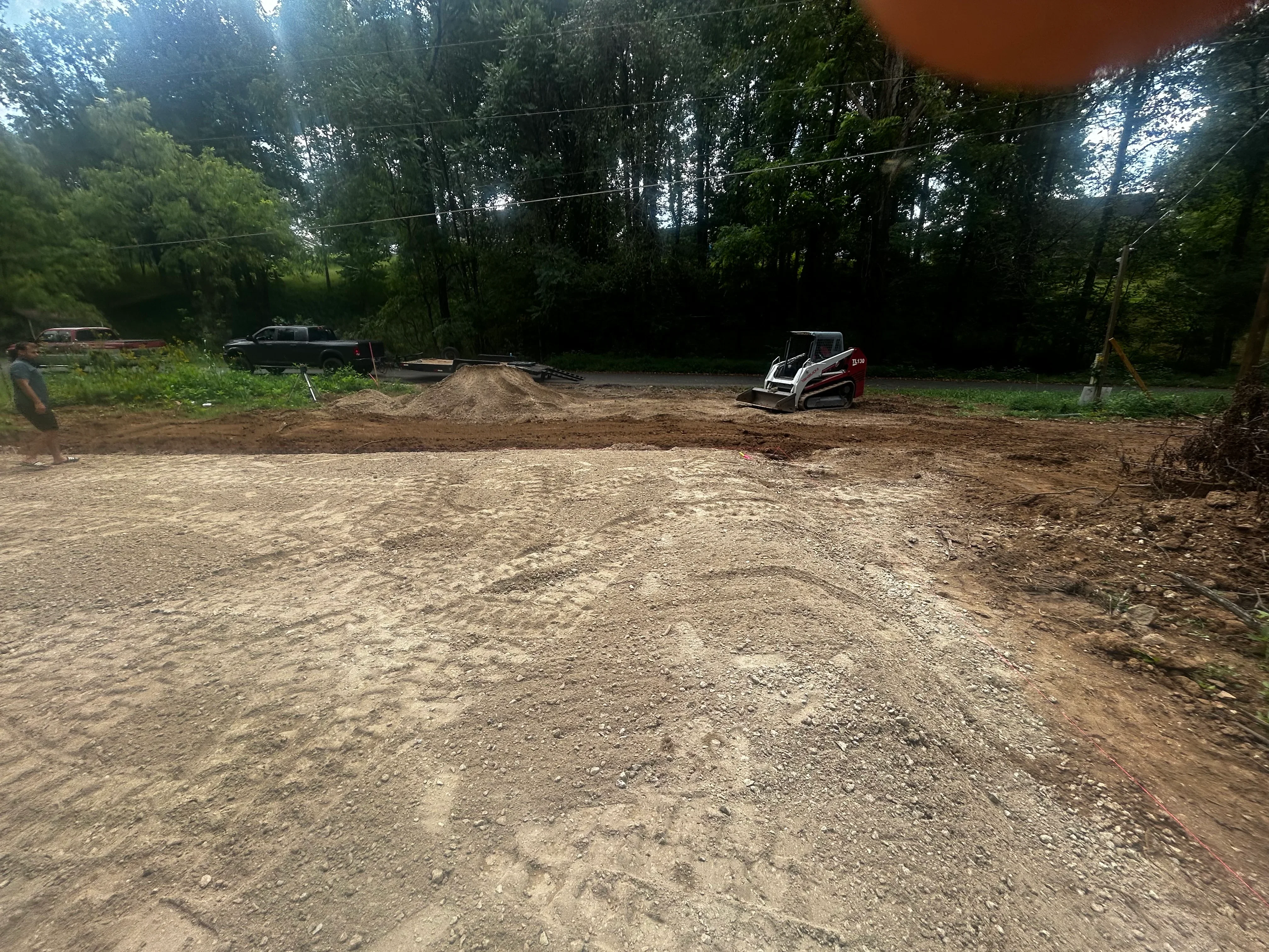 Graded driveway with compacted gravel, track loader, and cleared site surrounded by trees