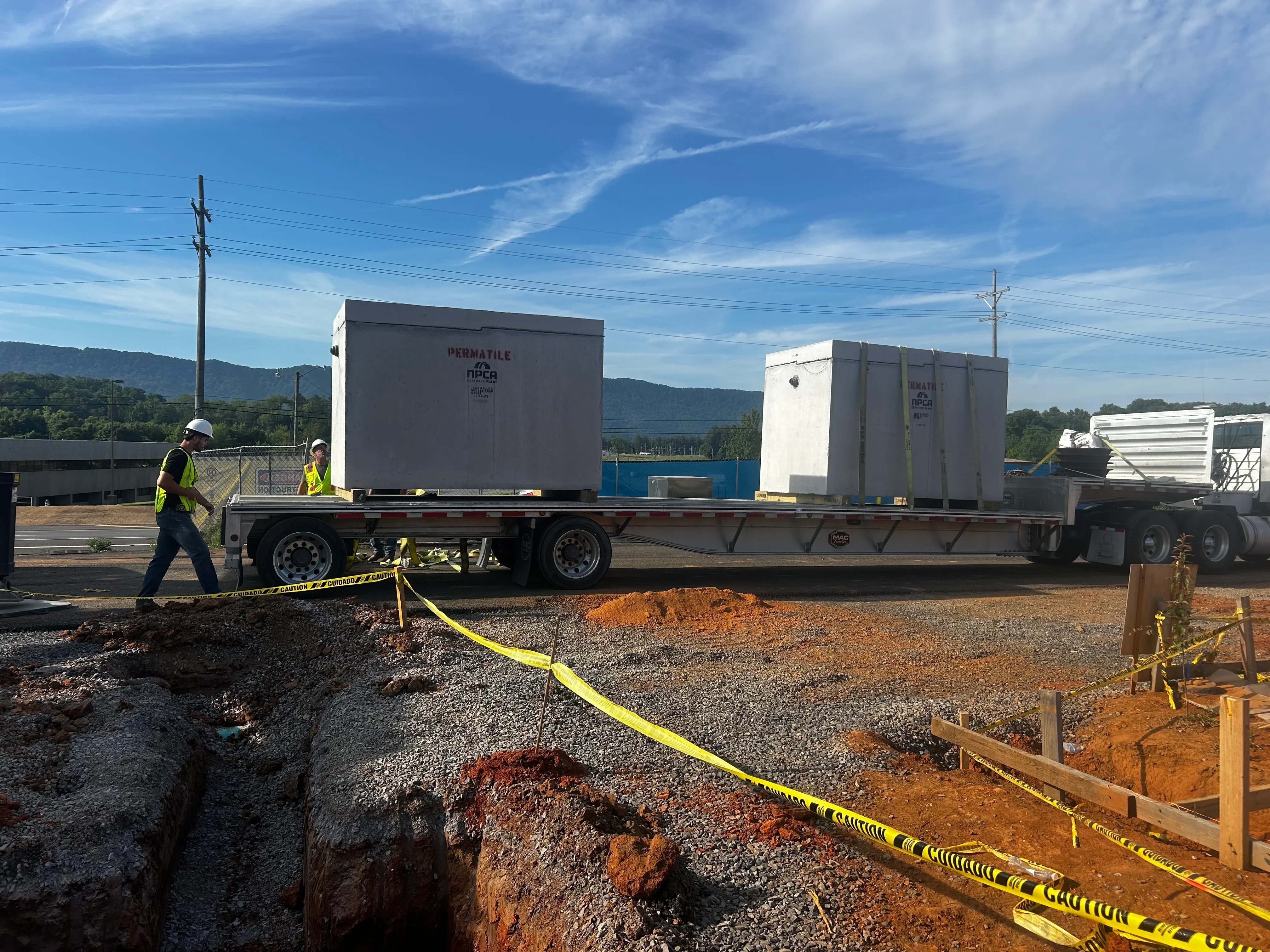 Septic tank delivery truck with workers positioning large concrete tanks on gravel foundation