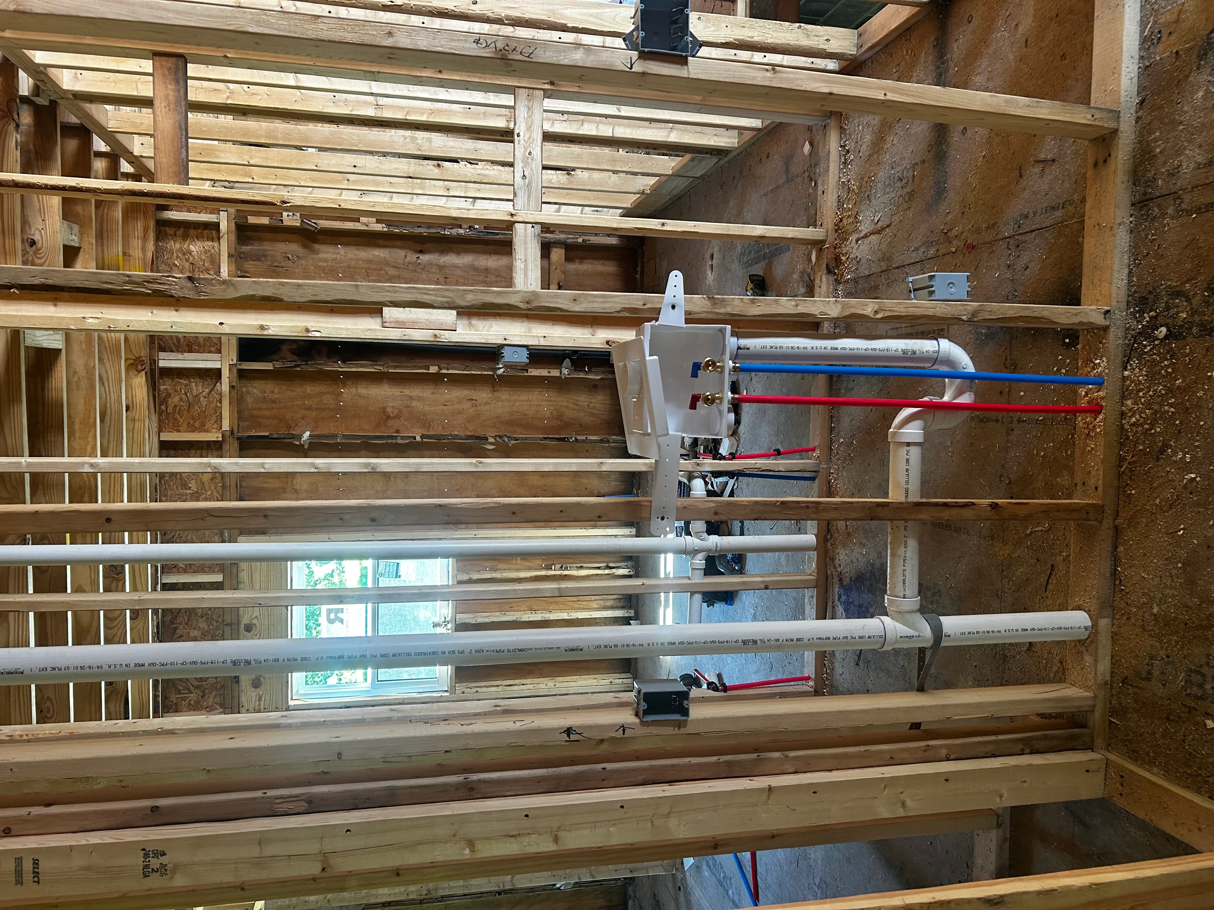 Plumbing rough-in with PVC and copper lines, color-coded tubing, manifold assembly in framed wall cavity