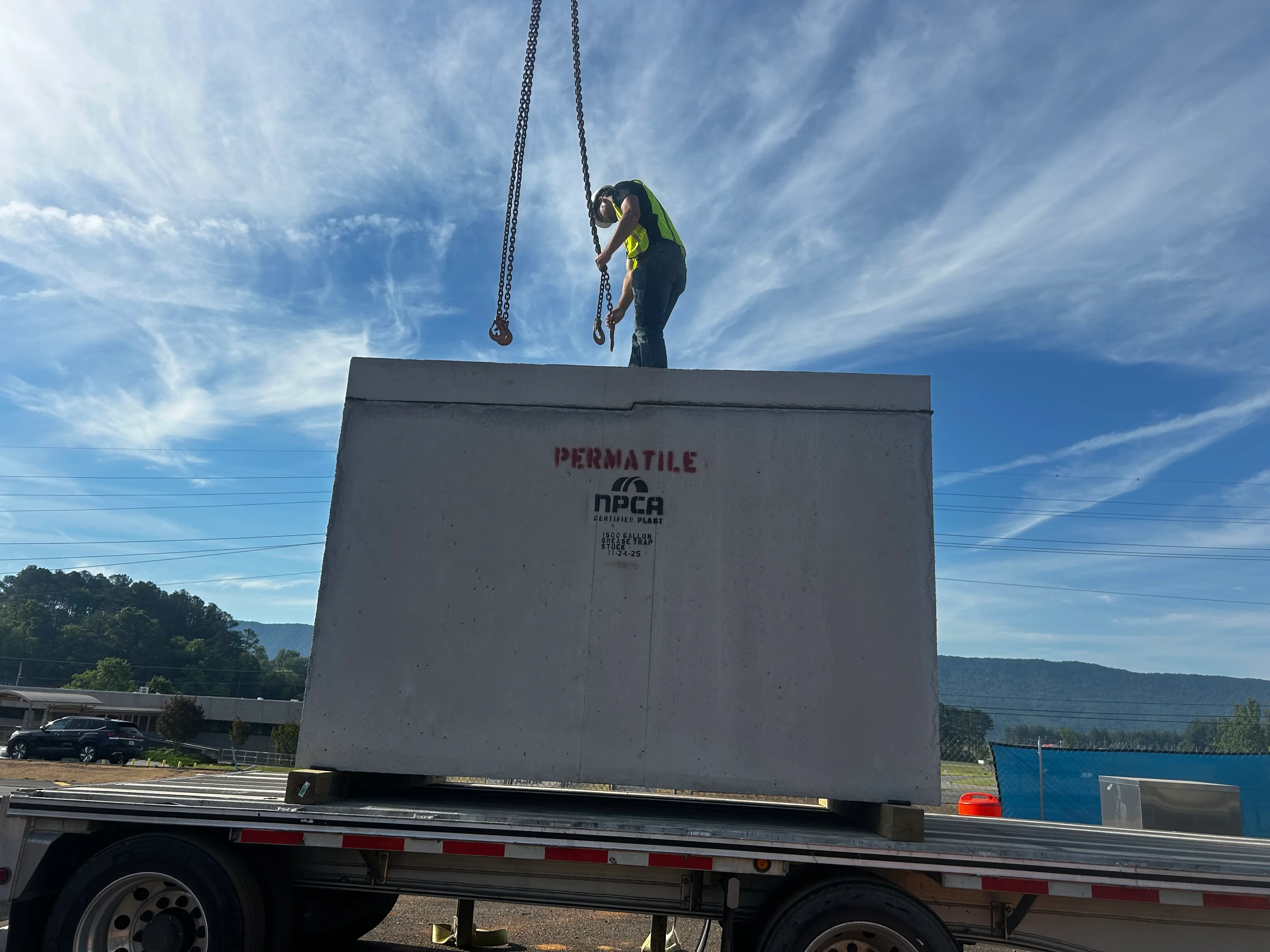 Crane operator positioning precast concrete septic tank with chains onto flatbed trailer