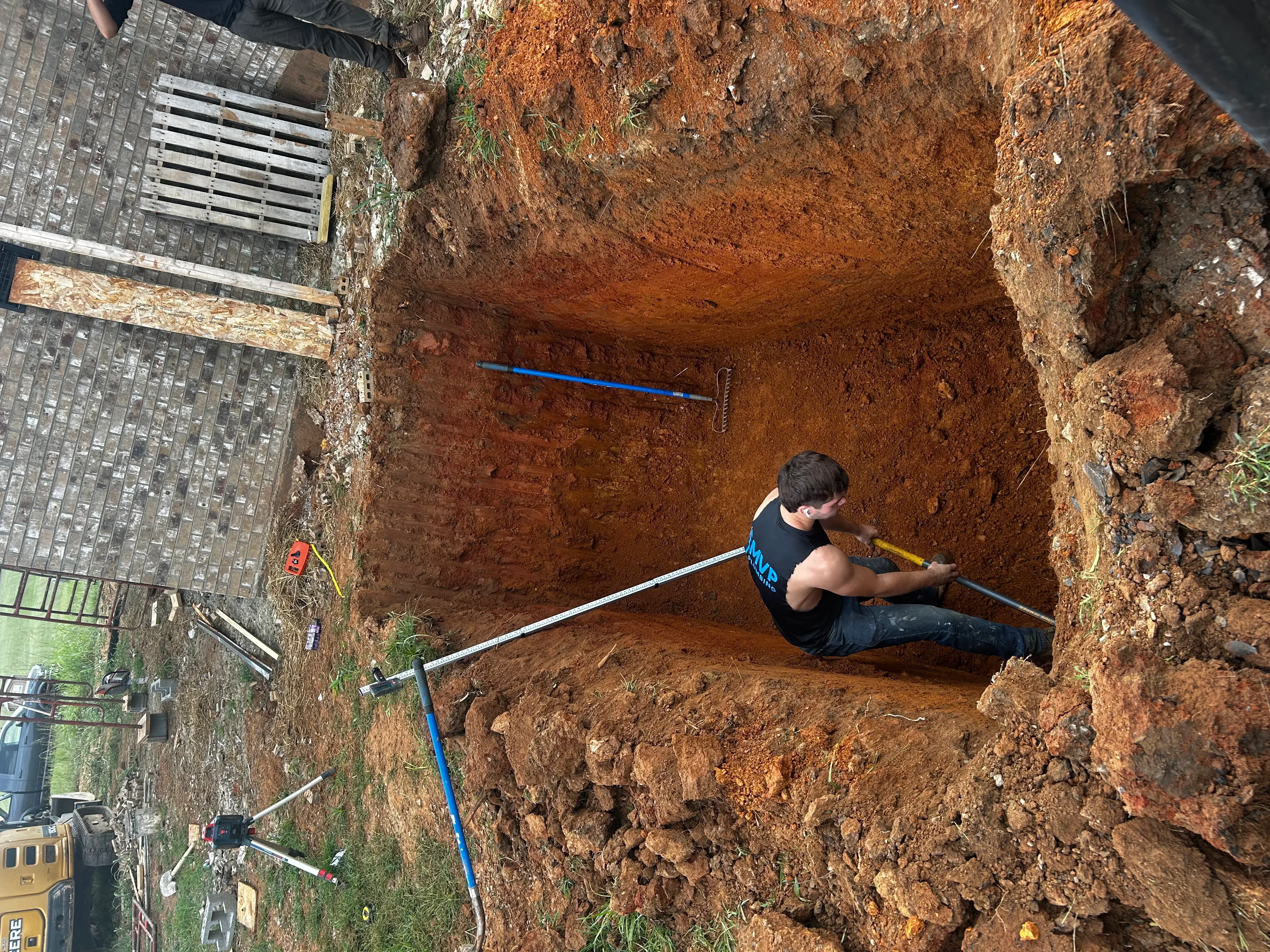Excavated septic system pit with blue PVC pipe and compacted soil walls