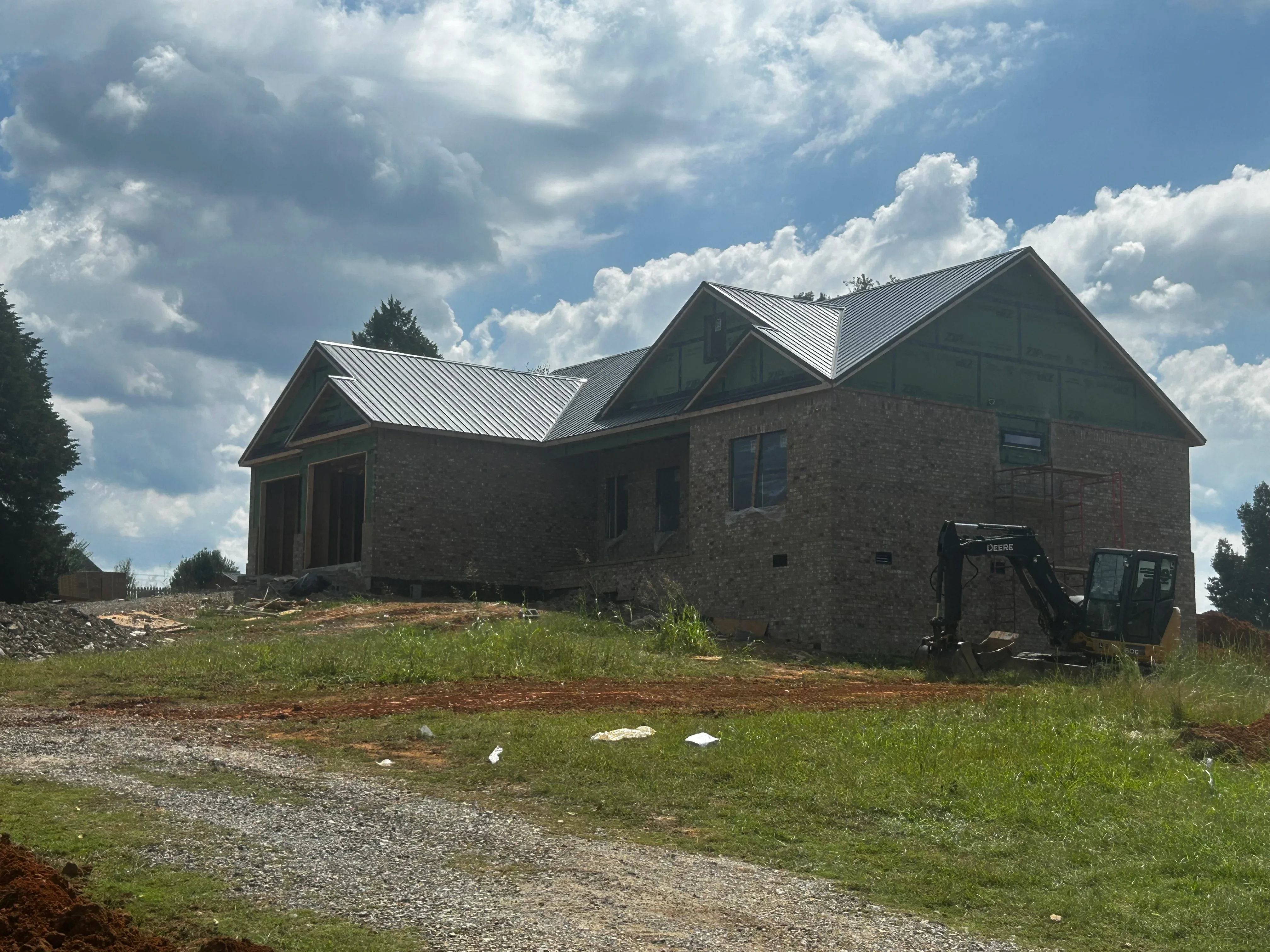 Brick home with metal roof during construction, septic system installation in progress with graded site