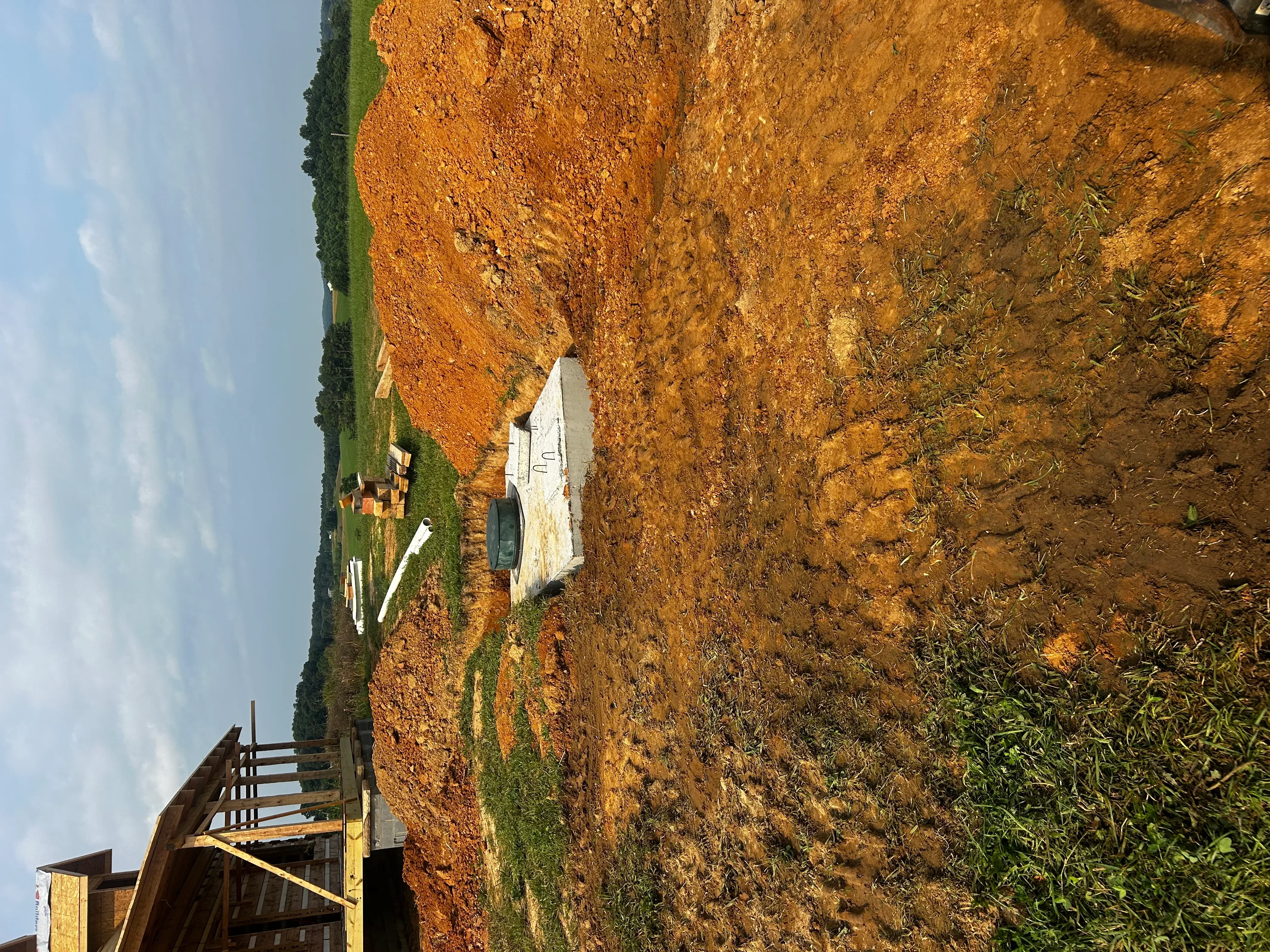 Excavated septic system installation site with clay soil, graded terrain, and white tank placement area