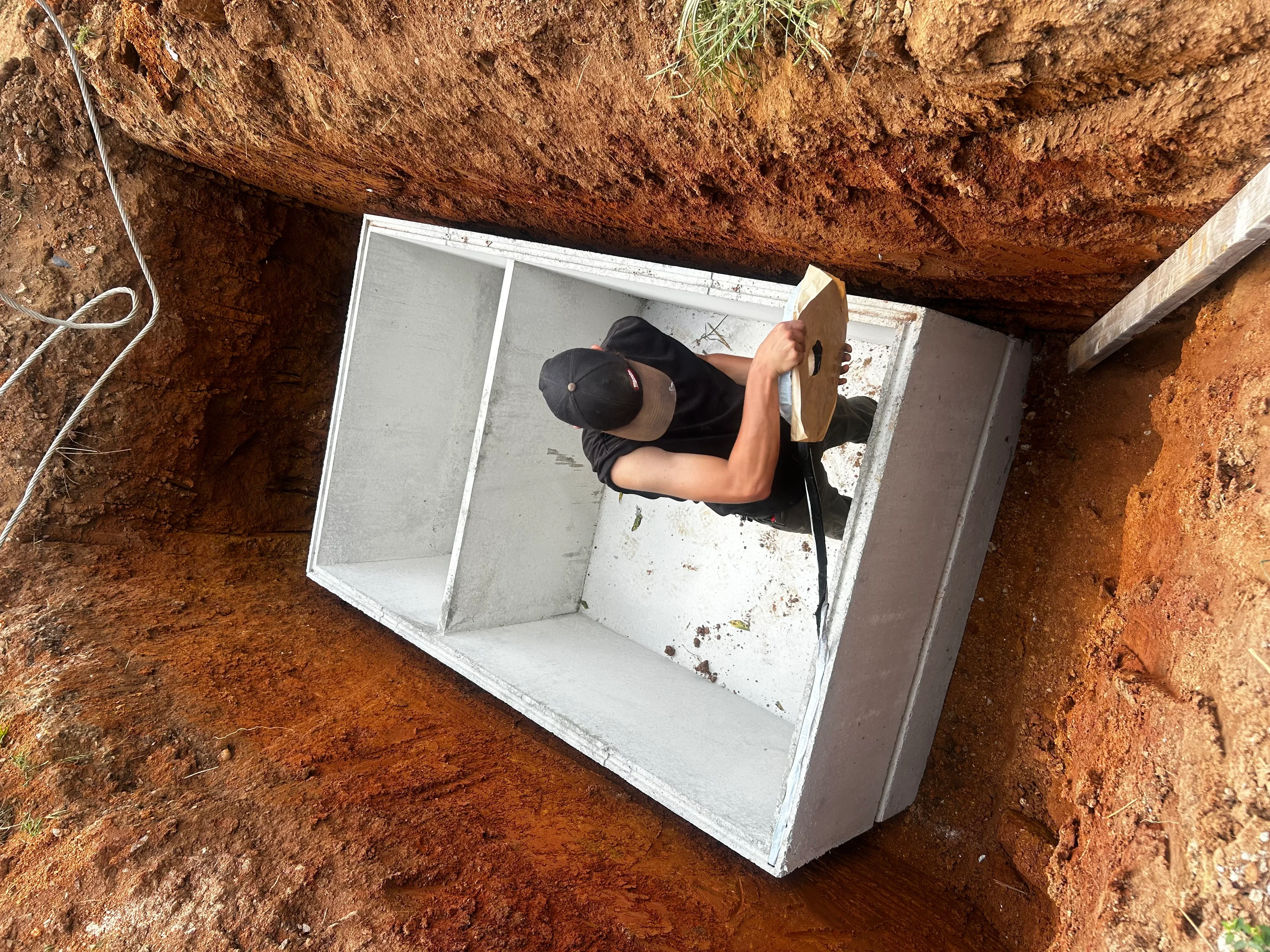 Concrete septic tank installed in excavated pit with internal compartments visible