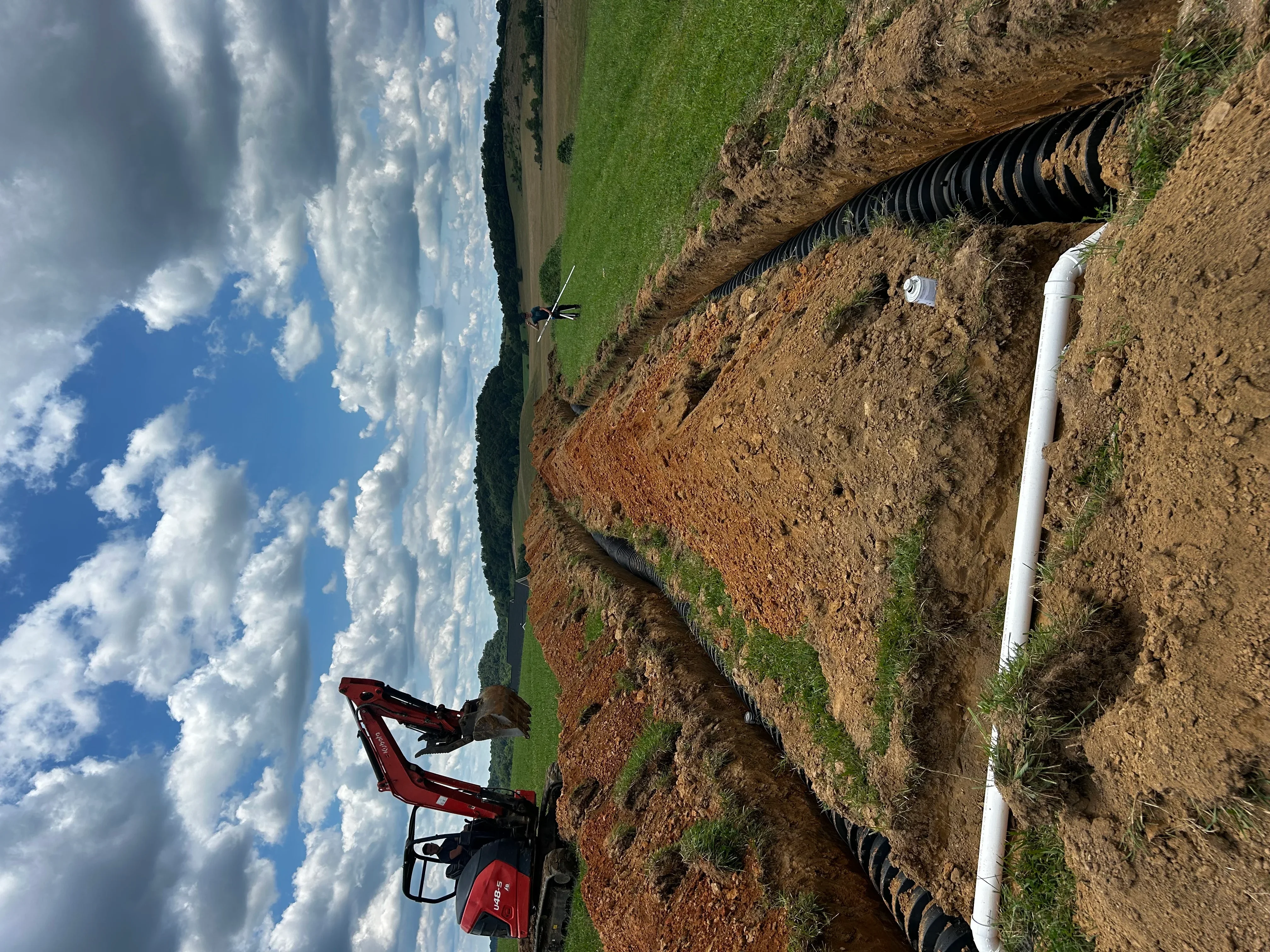 Septic system installation with black corrugated pipe and white PVC lines in excavated trench