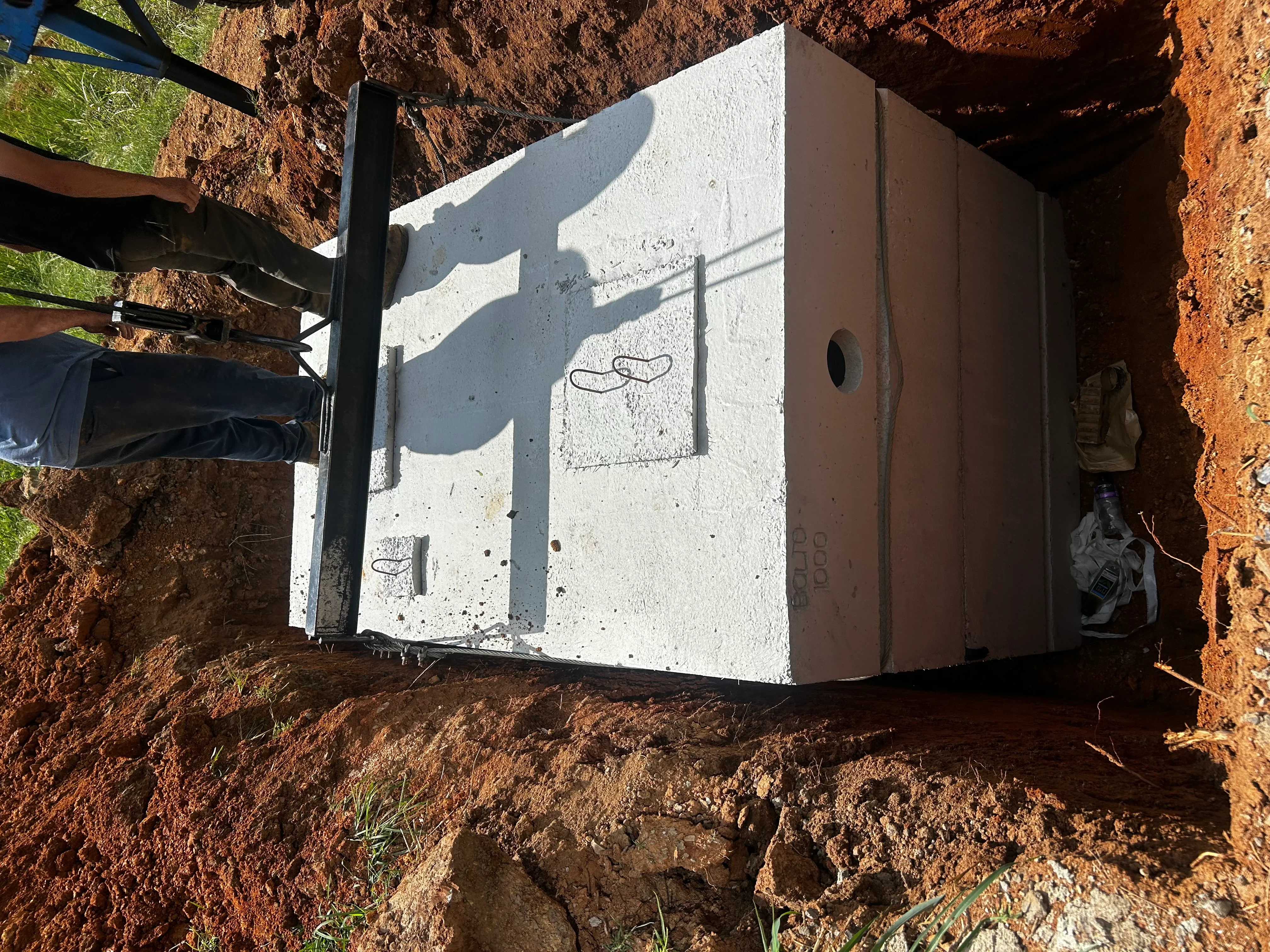 Concrete septic tank installed in excavated pit with metal support brackets and access ports
