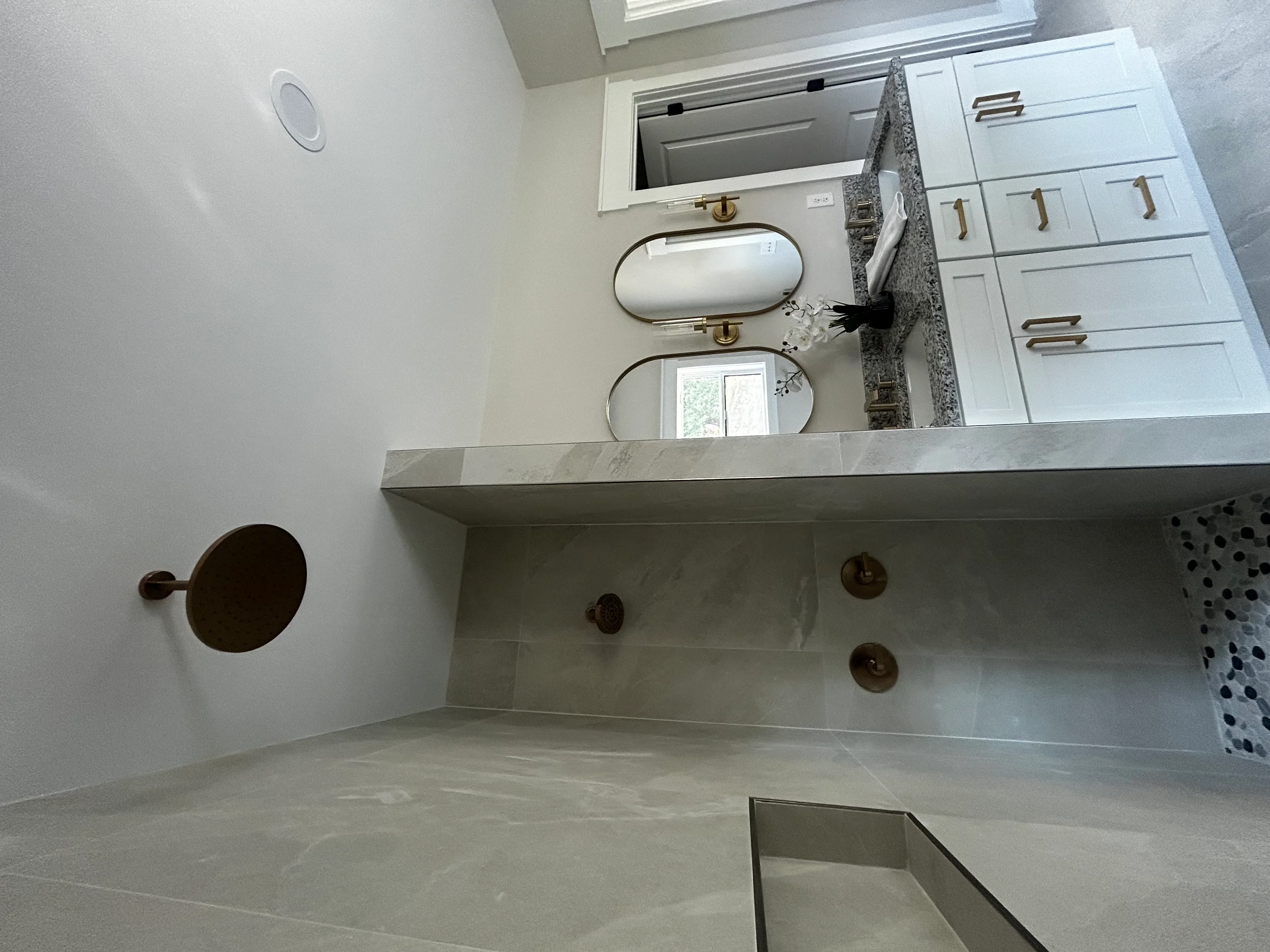Concrete vanity with dual sinks, brass mirrors, white cabinetry, and brass plumbing fixtures in modern bathroom