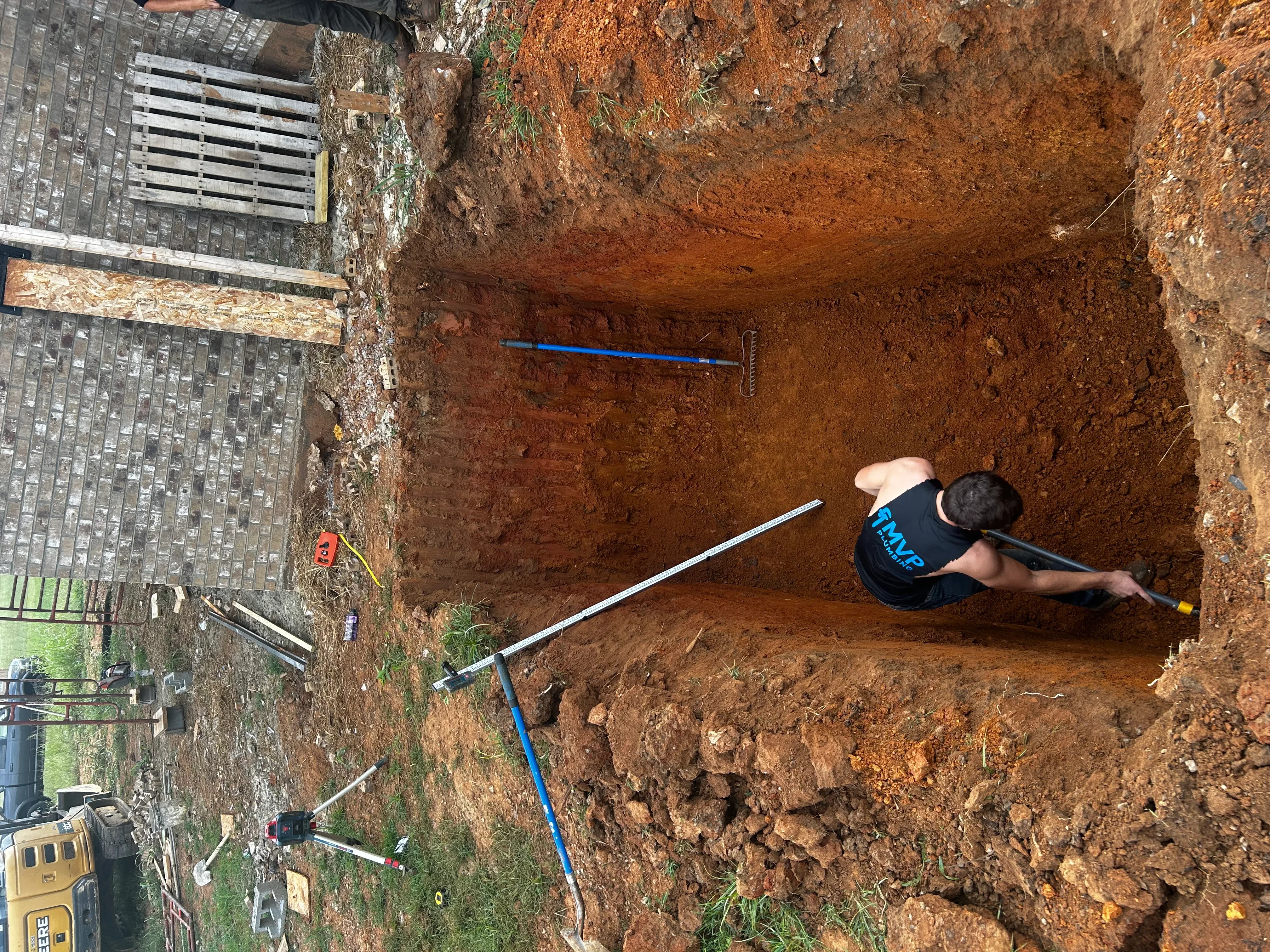 Excavated septic system trench with blue PVC pipe and measurement tools in clay soil