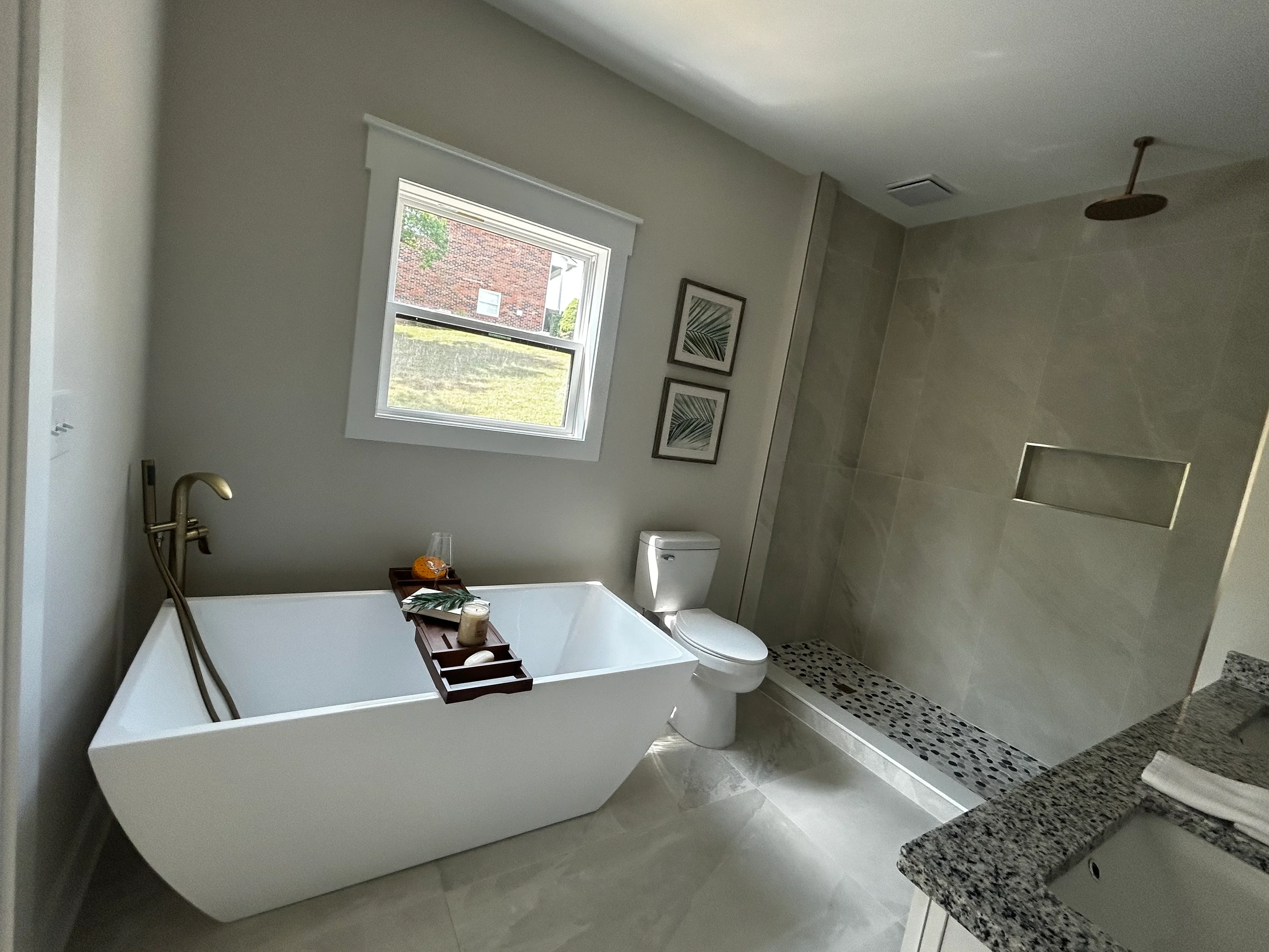 Freestanding white soaking tub, granite counters, tile shower with rainfall head, modern fixtures