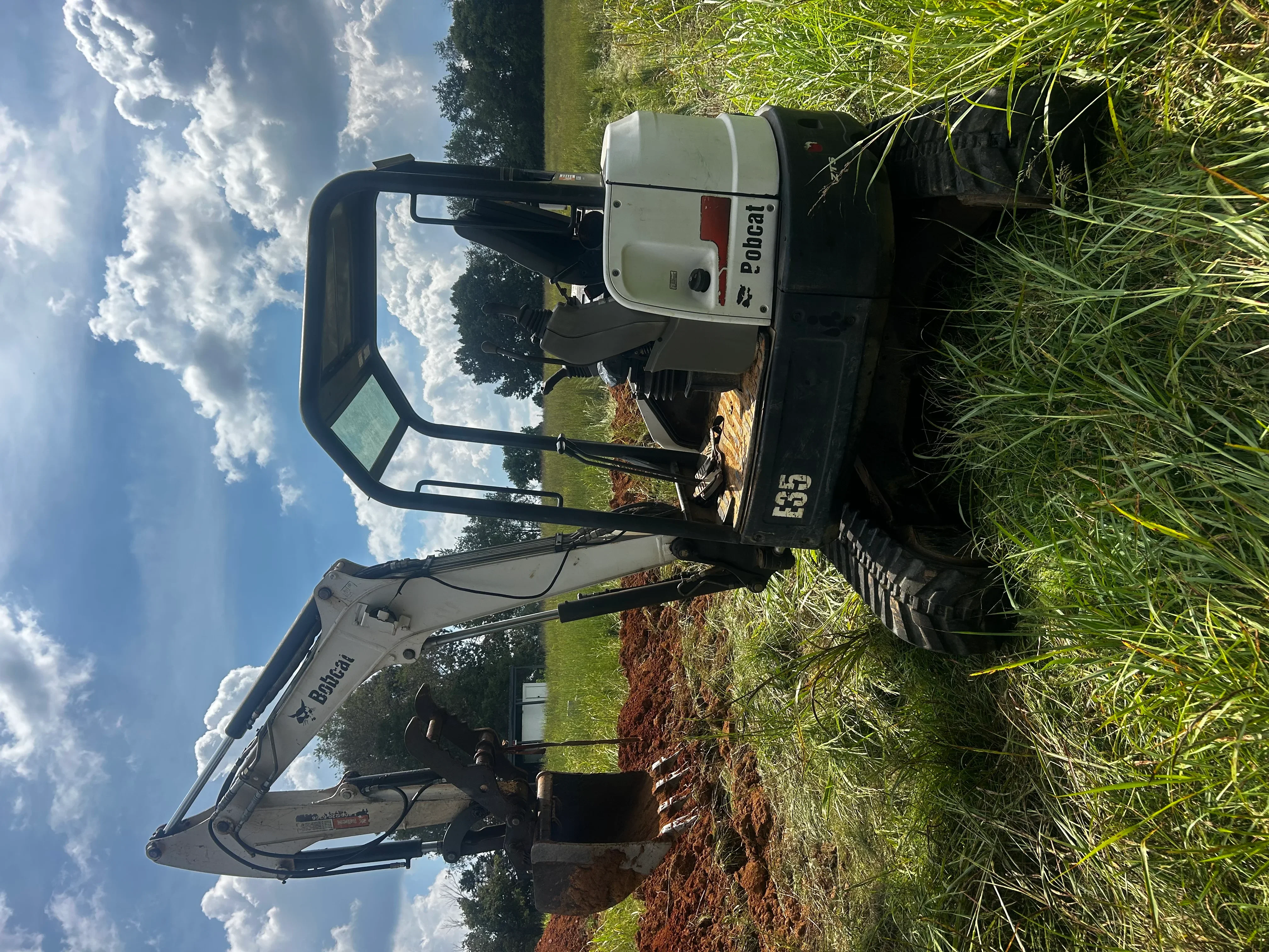 Bobcat mini excavator on job site with exposed soil and grass, septic installation work