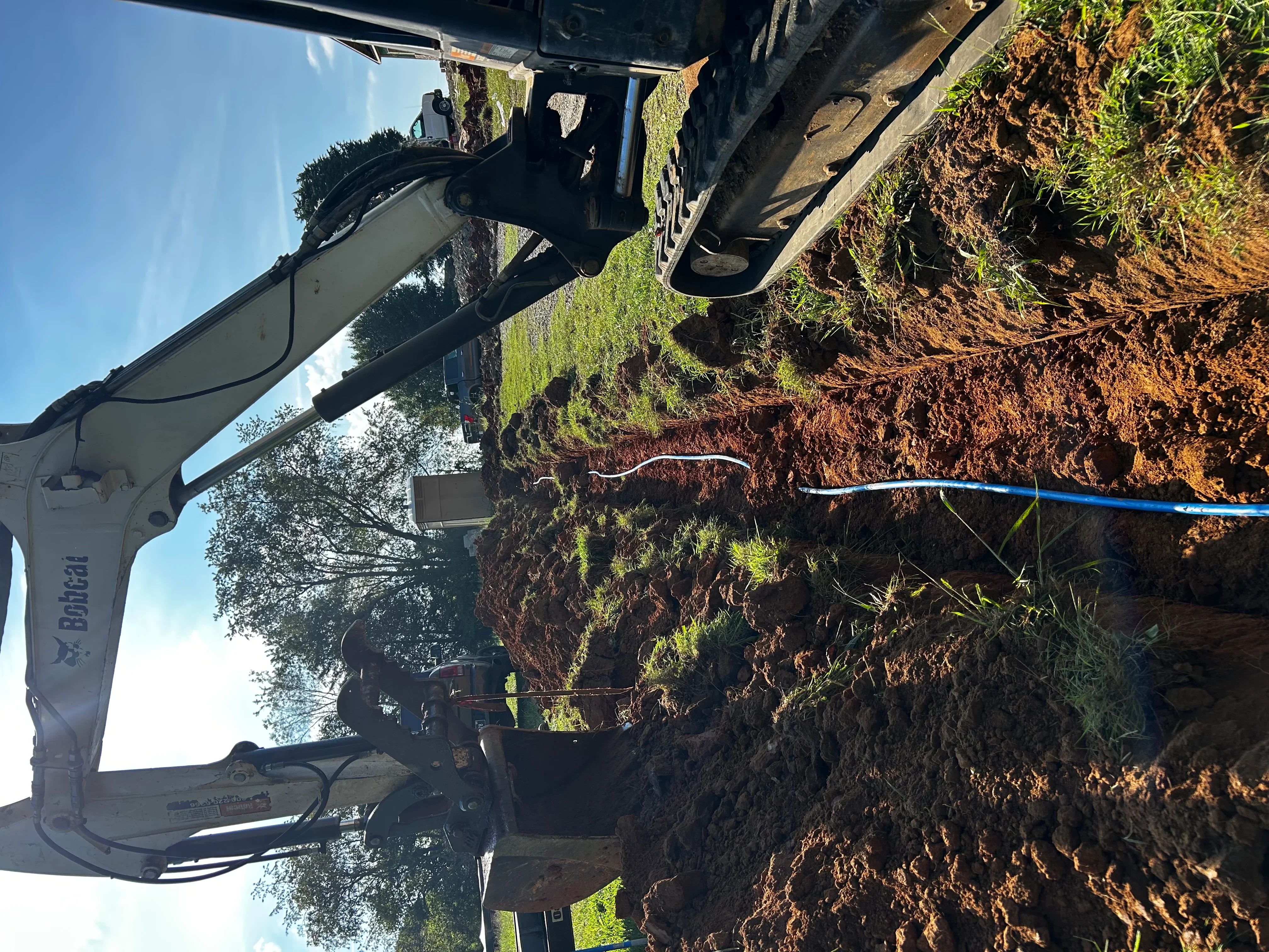 Bobcat excavator digging trench with blue PVC pipe for septic system installation